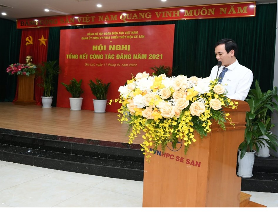 A person standing behind a podium with flowers in front of a red curtainDescription automatically generated with low confidence