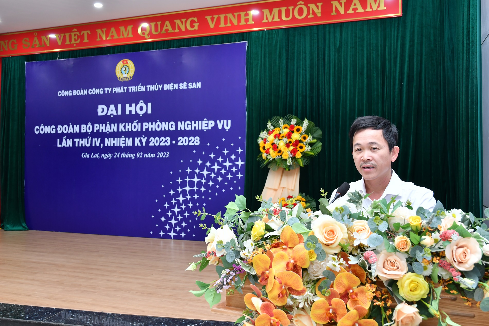 A person standing behind a podium with flowers in front of himDescription automatically generated with medium confidence