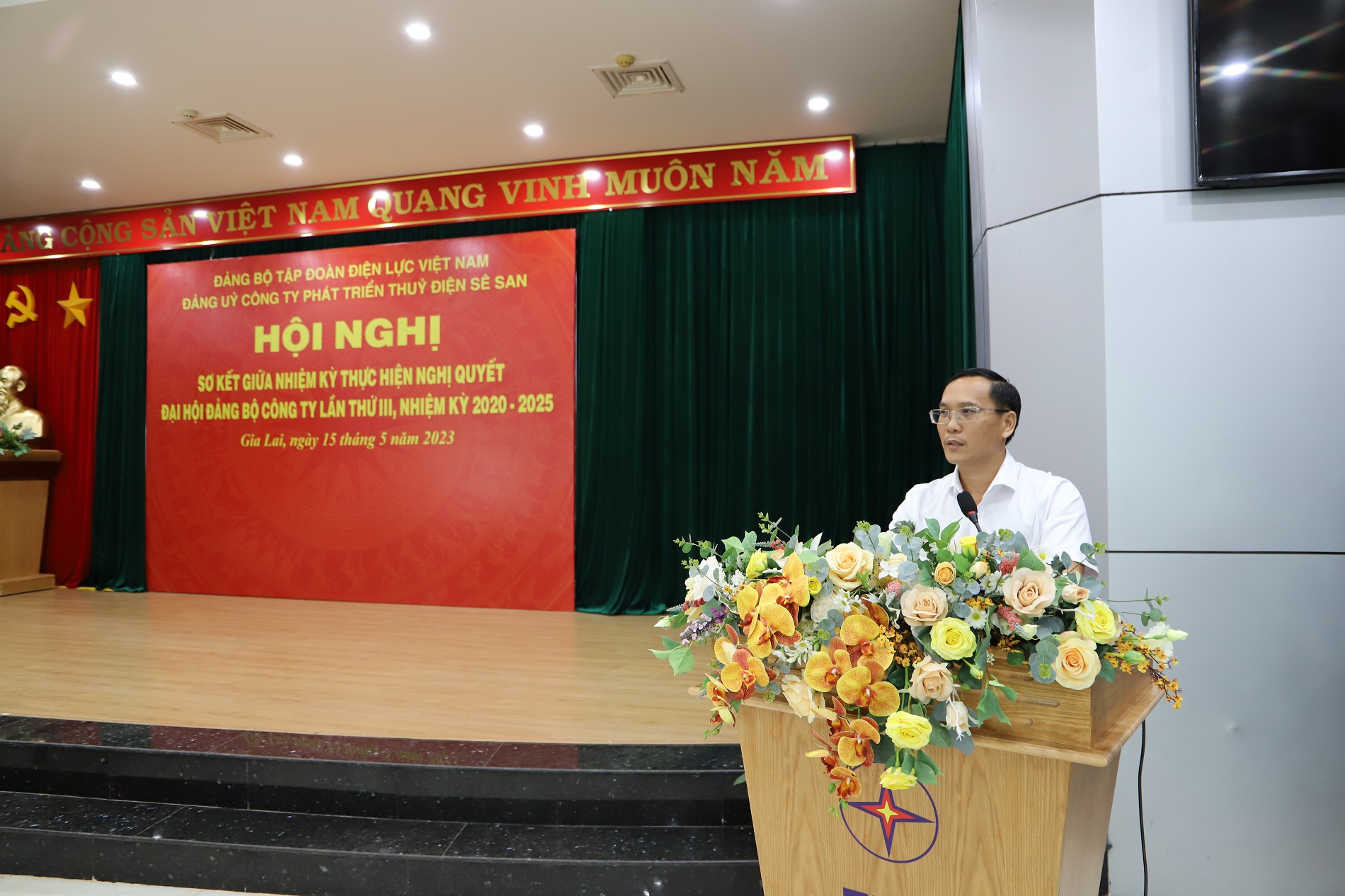 A person standing at a podium with flowersDescription automatically generated with medium confidence