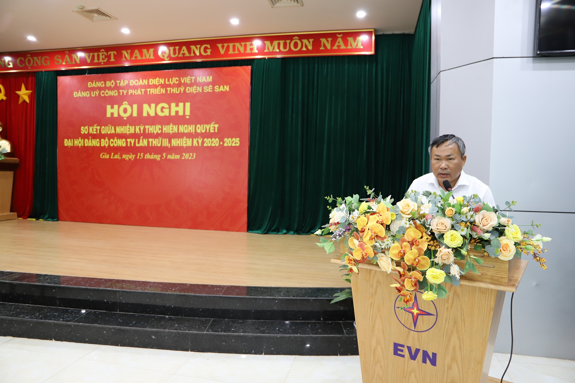 A person standing at a podium with flowersDescription automatically generated with low confidence