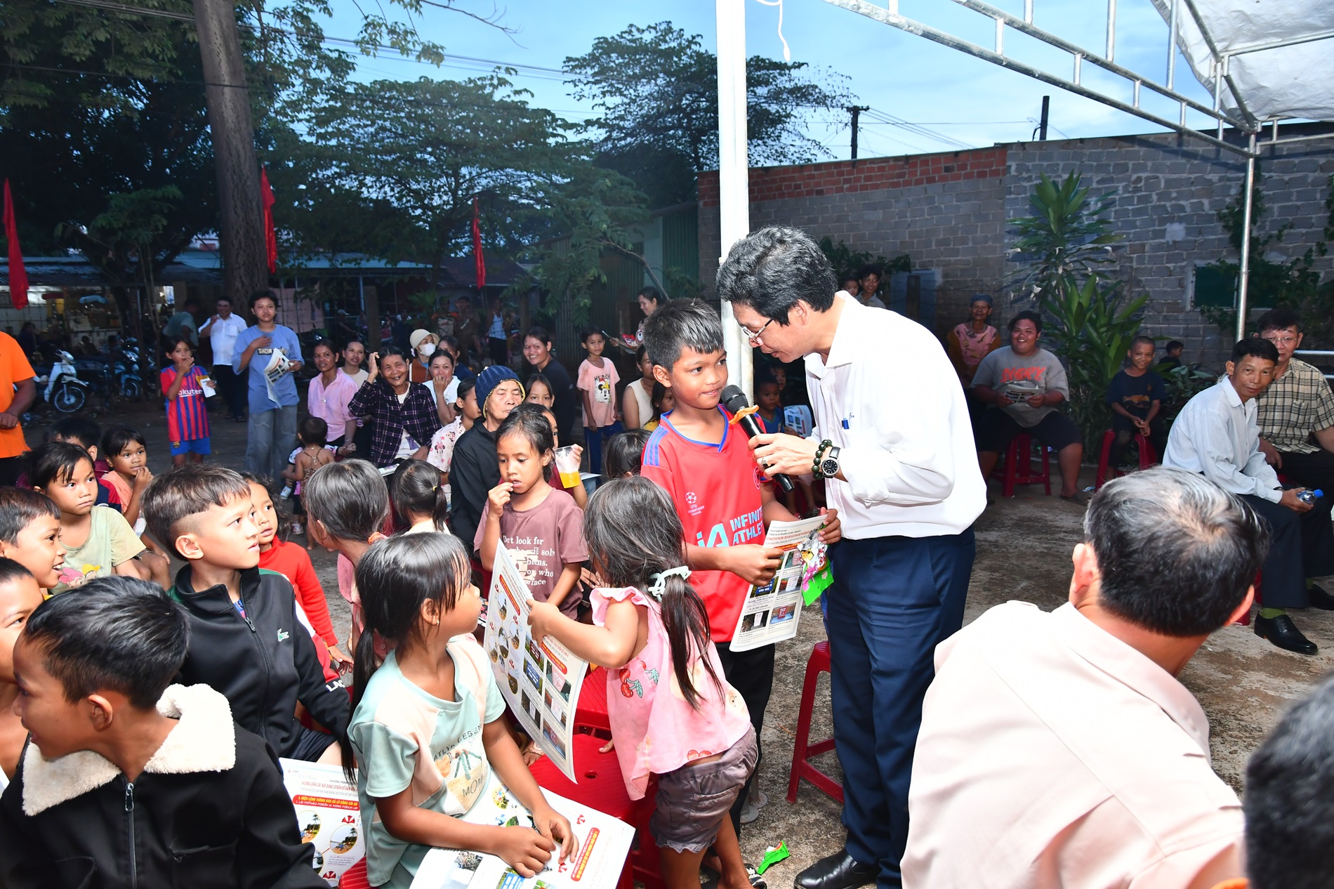 A person holding a microphone and standing next to a group of childrenDescription automatically generated