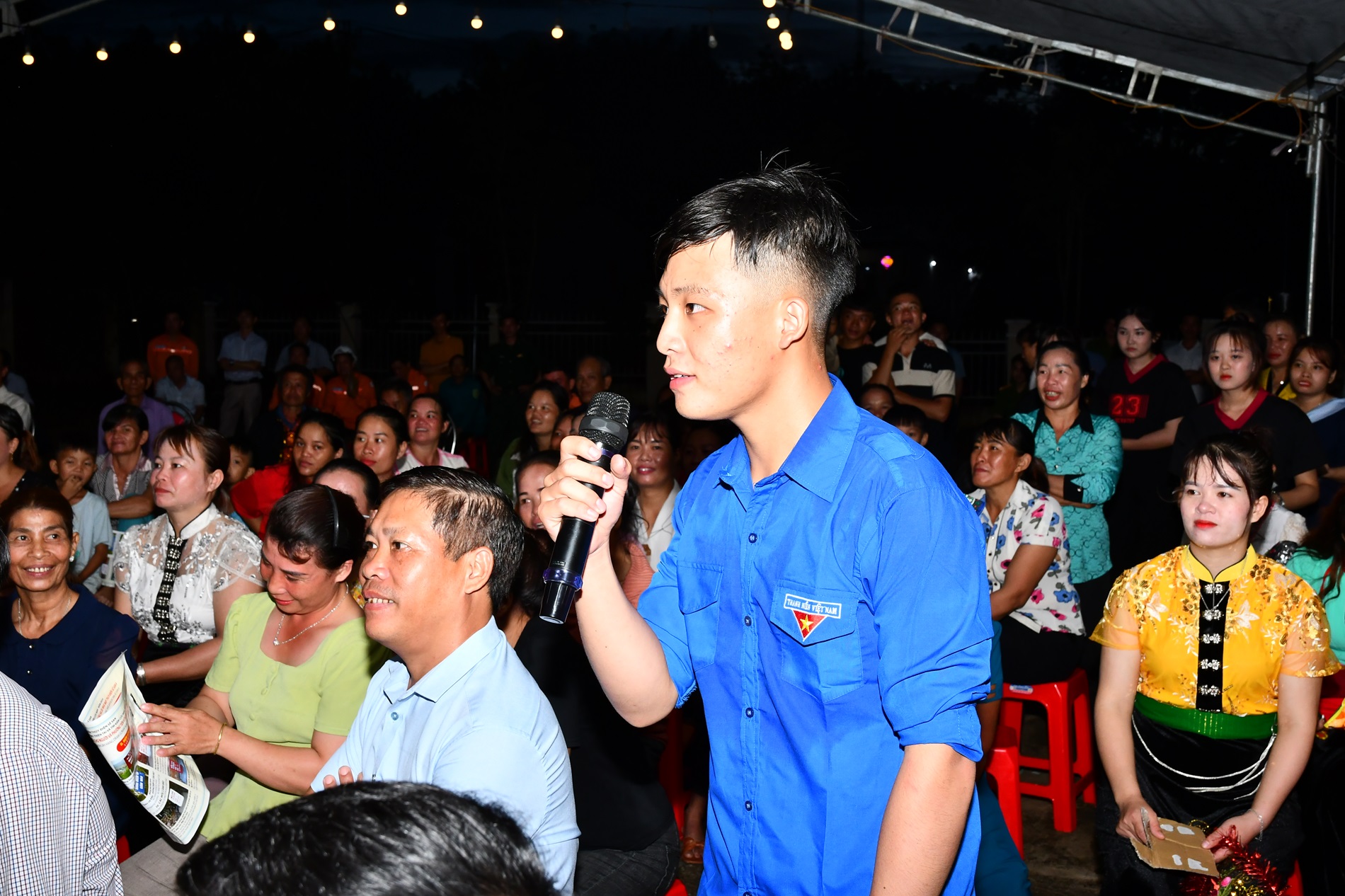 A person holding a microphone in front of a crowdDescription automatically generated